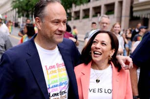 Doug Emhoff and Kamala Harris walk together in a pride parade. They are smiling and wearing shirts with pride-themed messages