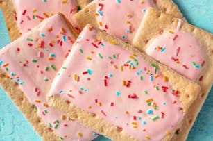 Several pink frosted toaster pastries with colorful sprinkles on a light blue surface